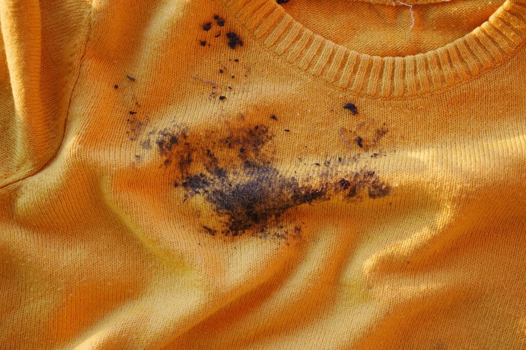 Stubborn grease stain on a yellow sweater, illustrating the challenges of stain removal and the importance of professional dry cleaning services.